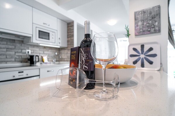 A modern kitchen with white cabinets, a microwave, and a wine bottle and glass on the counter.