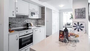 A modern kitchen with white cabinetry, a brick backsplash, and a countertop with a wine glass and bottle.