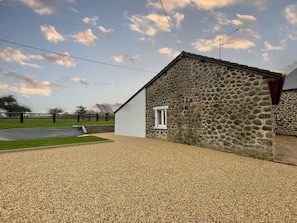 A stone building with a gravel driveway and a fenced area.