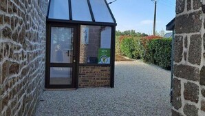 A small, single-story building with a sloped roof, a glass door, and a brick wall. - Charming granite house with enclosed garden, all inclusive, near Domfront (Saint-Mars-d'Égrenne)