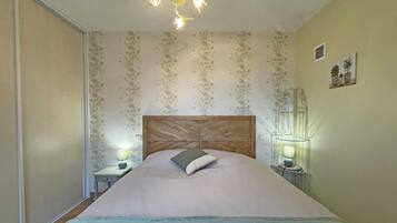 A bedroom with a wooden headboard, floral wallpaper, two bedside lamps, and a bed with a blue quilt.