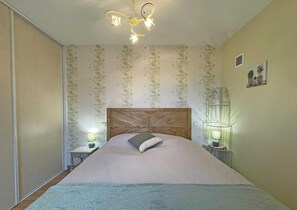 Une chambre à coucher avec une tête de lit en bois, un papier peint à motifs floraux, deux lampes de chevet et un lit recouvert d’une courtepointe bleue.