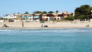 A beach with houses in the background and a person swimming in the water. - A-2 Loft Veranda sea view 1st row 1st floor (Fondo Morte)