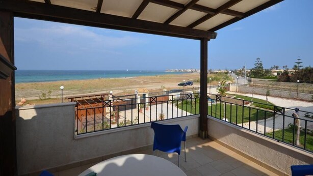 A balcony with a view of the beach and ocean, a table, and a blue chair. - A-2 Loft Veranda sea view 1st row 1st floor (Fondo Morte)