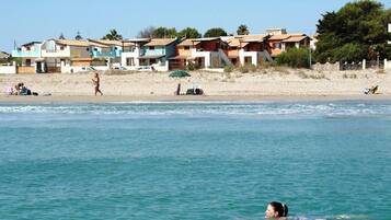 Ein Strand mit Häusern im Hintergrund und einer Person, die im Wasser schwimmt.