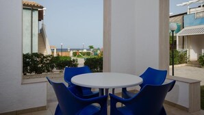 A patio area with a round table and blue chairs, overlooking a playground and buildings.