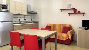 A compact kitchen with a dining table and chairs, a sofa, and a small TV.