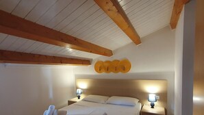 Un dormitorio con techo de madera, una cama con ropa de cama blanca, dos lámparas de noche y un aplique de pared.
