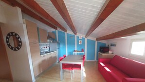 Una cocina con una mesa de comedor y sillas rojas, un sofá rojo y un televisor en la sala.