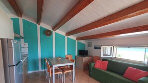 A kitchen with a refrigerator, a dining table with chairs, a green sofa with red cushions, and a television on a small table. - Apartment in attic B2 first row (Fondo Morte)