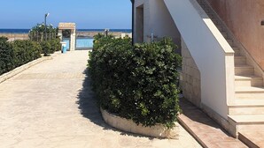 A building with a staircase leading to a balcony overlooking a beach. - Apartment in attic B2 first row (Fondo Morte)