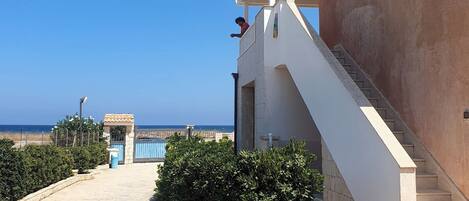 A building with a staircase leading to a balcony overlooking a beach.