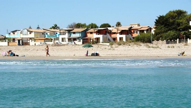 A beach with houses in the background and a person swimming in the water. - Apartment in attic B2 first row (Fondo Morte)