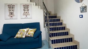 A staircase with a metal railing, a blue sofa with patterned cushions, and two framed artworks on the wall. - Apartment D2 sea view first floor (Marzamemi)