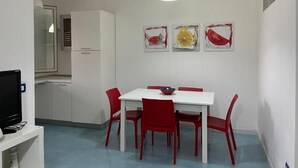 A compact kitchen with a white table and red chairs, a white ceiling light, and three framed artworks on the wall. - Apartment D2 sea view first floor (Marzamemi)