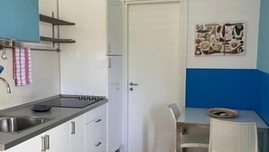 Kompakti keittiö, jossa on pesuallas, työtaso ja kaapistot. Keittiössä on myös ruokailutila, jossa on pöytä ja tuolit.