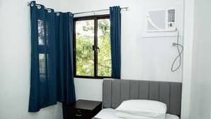 Een slaapkamer met een bed, een nachtkastje, een raam met gordijnen en een airconditioning.