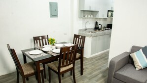 Een eetruimte met een houten tafel gedekt voor vier personen, omringd door stoelen. Achtergrond toont een keuken met witte kasten en een granieten aanrecht.