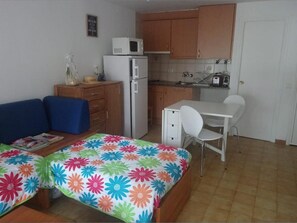 A compact room with a bed, a desk, a chair, a microwave, a refrigerator, and wooden cabinets.