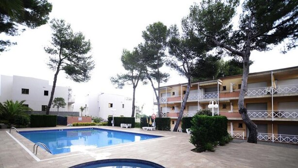 Une piscine avec une petite partie circulaire, entourée d’arbres et bordée d’un immeuble à plusieurs étages doté de balcons.