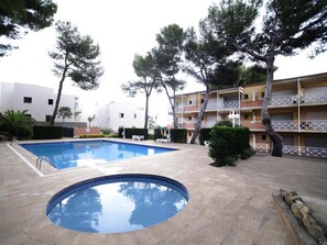 A swimming pool with a small circular section, surrounded by trees and a multi-story building with balconies.