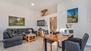 Ett modernt vardagsrum med en soffa, ett soffbord och ett matbord. Det finns tavlor på väggarna och en tv som är monterad på väggen.