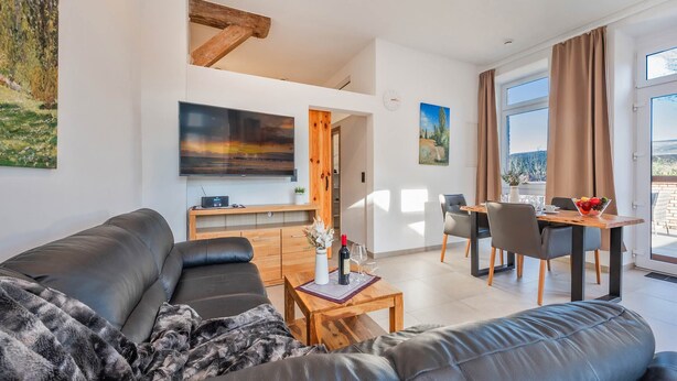 Ett modernt vardagsrum med en svart lädersoffa, ett träbord som soffbord och en matplats med ett träbord och stolar.