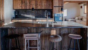 A modern kitchen with wooden accents, a central island, bar stools, and a built-in oven. - Luxury 10 person, 5 bedroom chalet with hot tub, sauna and steam room. (Landry)