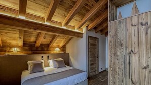 A bedroom with a wooden ceiling, a bed with white bedding, and a wardrobe with a wooden finish. - Luxury 10 person, 5 bedroom chalet with hot tub, sauna and steam room. (Landry)