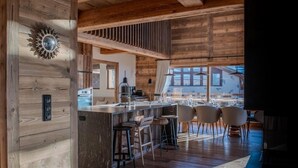 A modern kitchen with a wooden interior, a bar area with stools, and a view of the outside. - Luxury 10 person, 5 bedroom chalet with hot tub, sauna and steam room. (Landry)