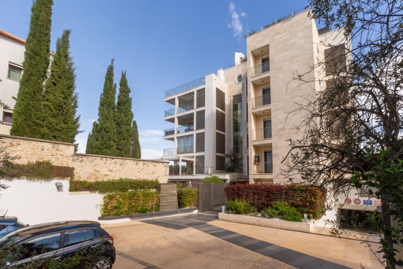 Un edificio moderno con appartamenti, diversi balconi, un'area parcheggio e vegetazione circostante.