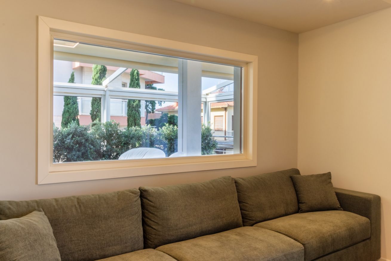 Un soggiorno con un'ampia finestra, un divano beige e vista su una zona residenziale.