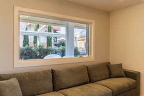 A living room with a large window, a beige couch, and a view of a residential area. - TERRAZZA61 - Apartment with an amazing views of the city of Cagliari (Cagliari)