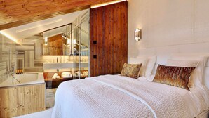 Un dormitorio moderno con una cama grande, un revestimiento de pared de madera, una cabina de ducha de vidrio y un tocador de baño blanco.