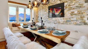 Un comedor con una mesa de madera dispuesta para seis personas, un sofá blanco y una pared de piedra con una obra de arte colorida.