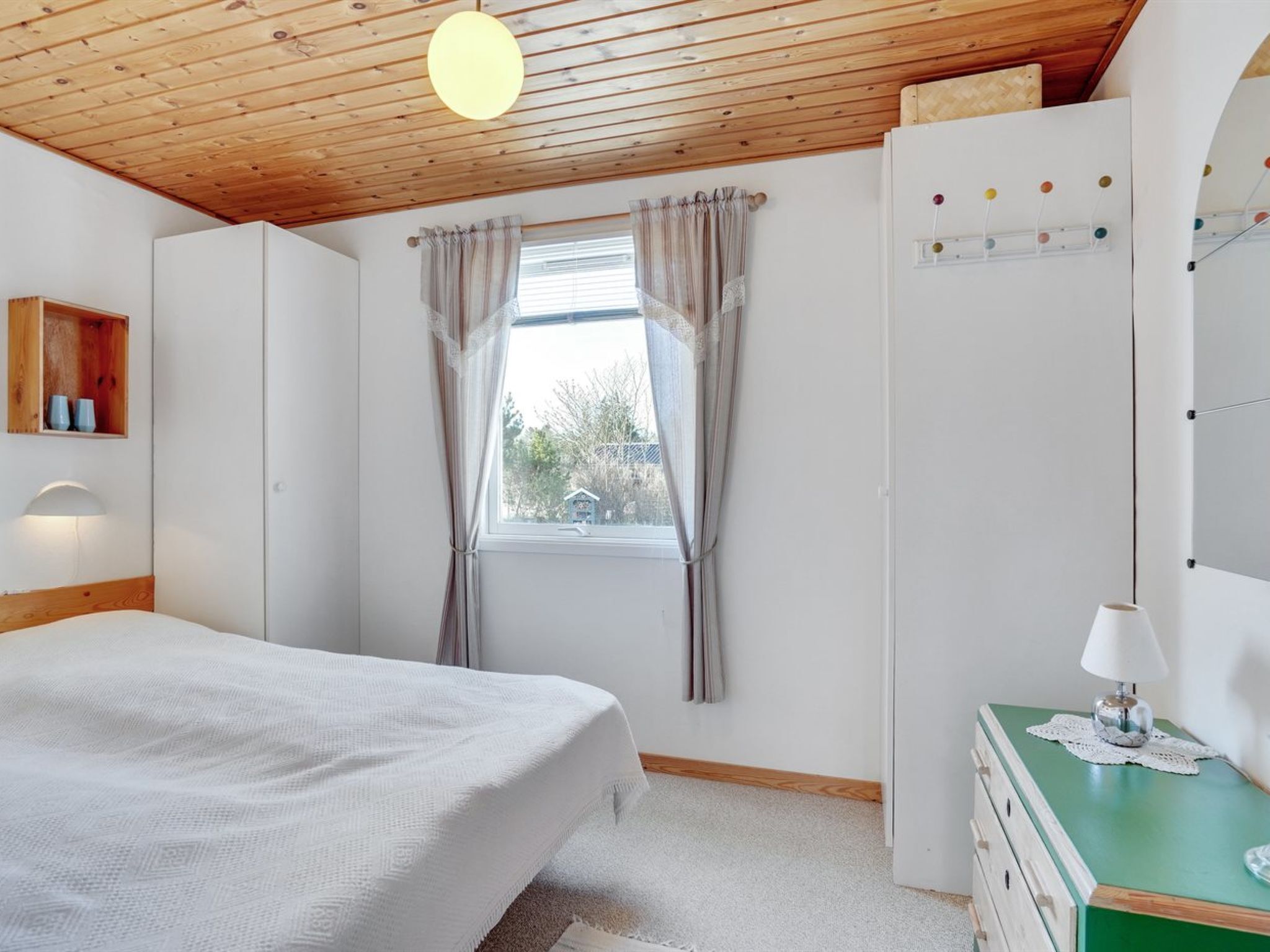Una camera da letto con soffitto in legno, un letto, una cassettiera e una finestra con tende.