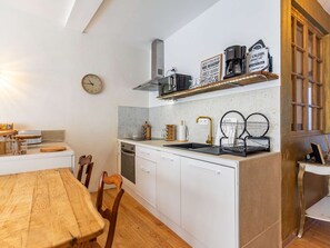 Una cocina compacta con armarios blancos, una mesa de comedor de madera y un reloj en la pared.