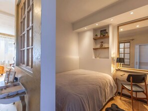 Un dormitorio con cama, escritorio, silla, espejo y estantes decorados con objetos ornamentales.