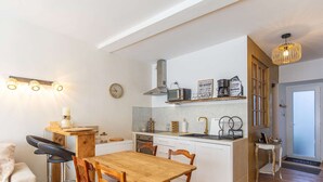 Une cuisine compacte avec une table et des chaises en bois, un petit tabouret de bar et une horloge au mur.