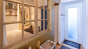 Une pièce avec une grande fenêtre, une porte dotée d’un paillasson et une petite table sur laquelle se trouvent divers objets.