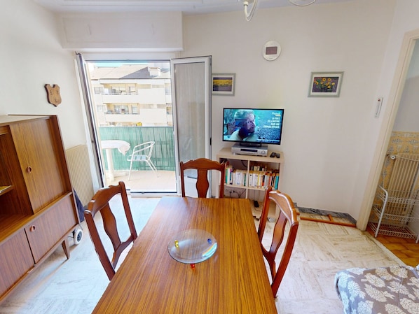 A dining area with a wooden table and chairs, a television, and a view of a balcony with buildings.