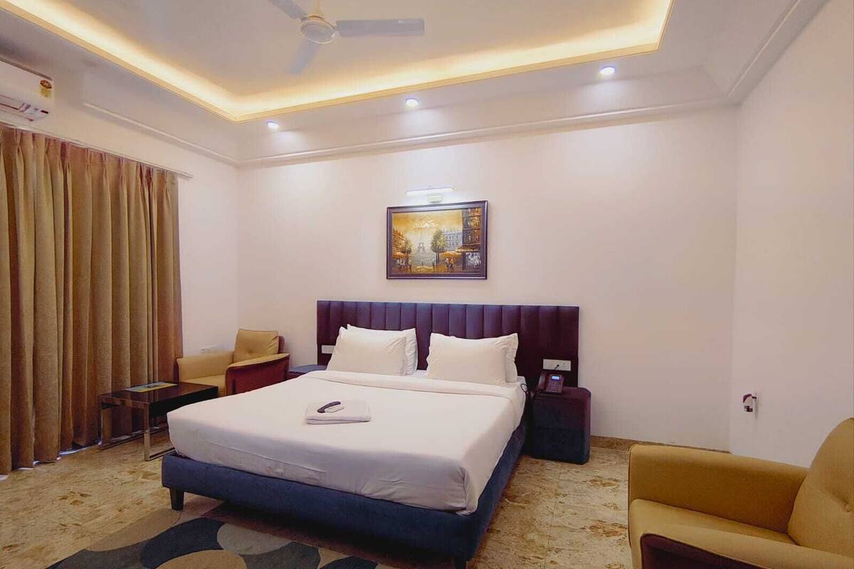 A hotel room with a large bed, a ceiling fan, a painting on the wall, and a desk with a chair.