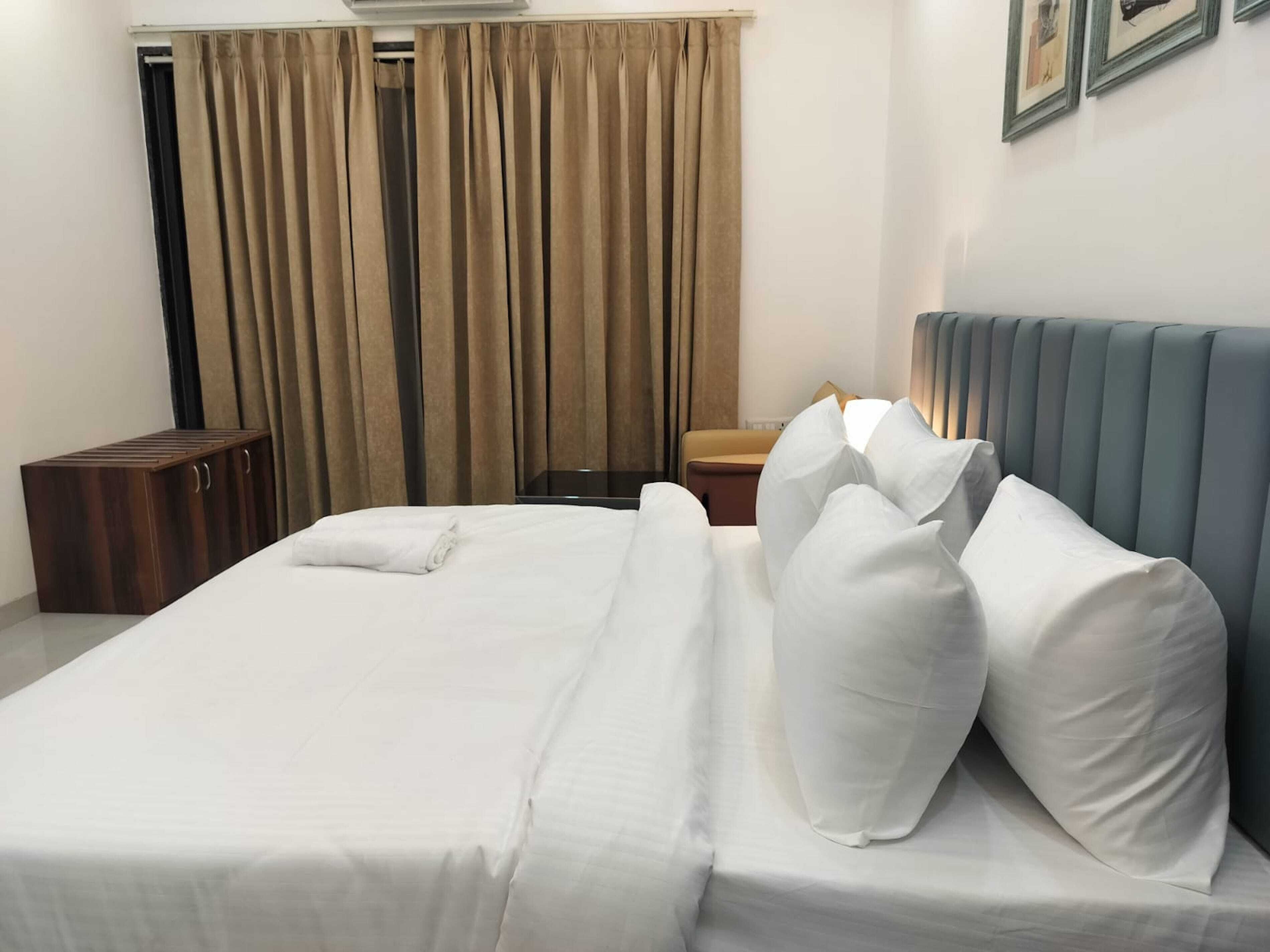 A neatly made bed with white linens and pillows, a wooden bench, and a headboard with vertical panels.