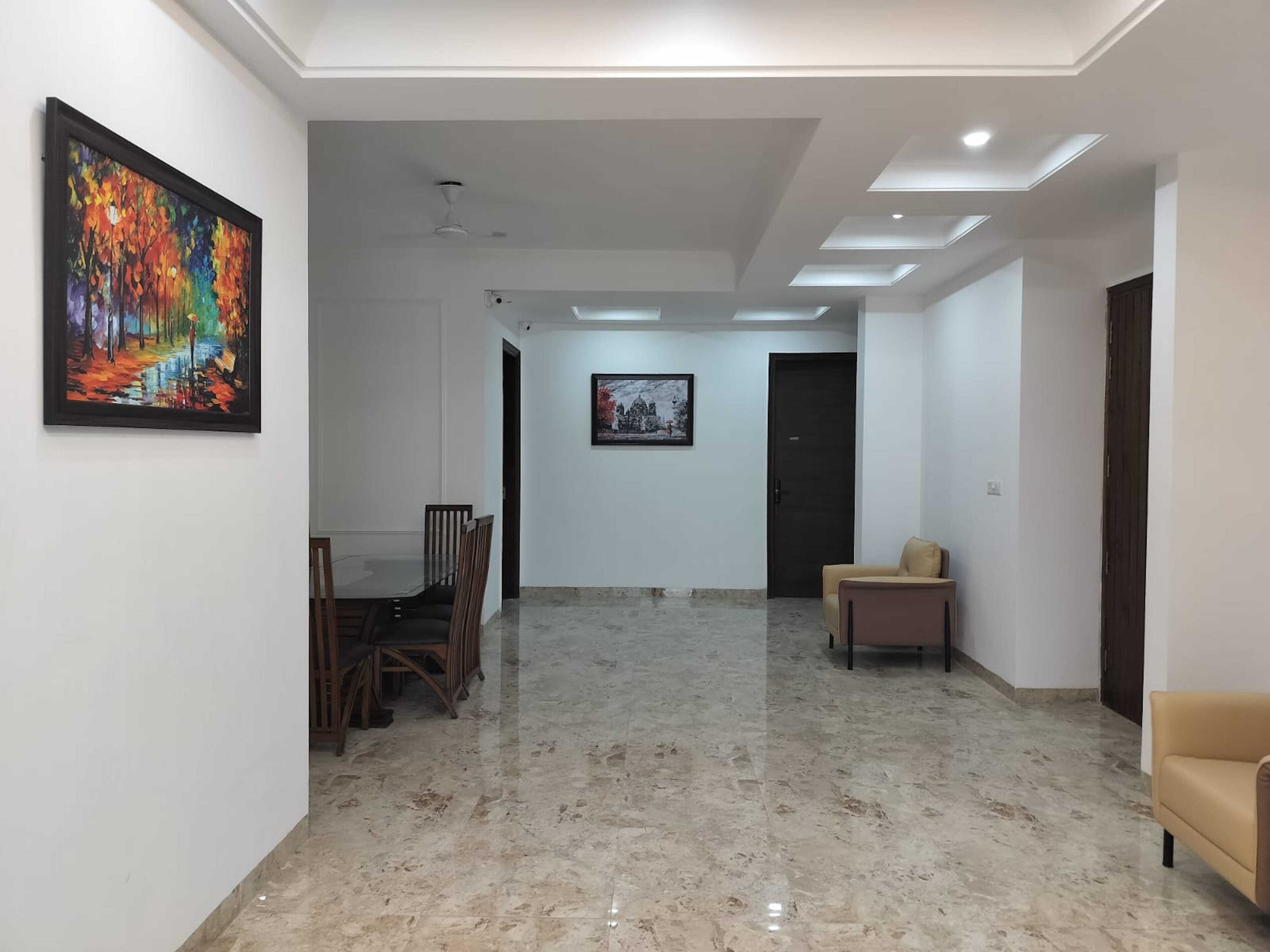 Un pasillo amplio con piso de mármol, una zona de comedor con sillas de madera y dos obras de arte enmarcadas en las paredes.