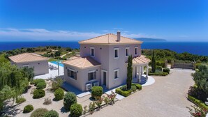 Una villa grande de varios pisos con piscina, rodeada de jardines ajardinados y vista al mar.