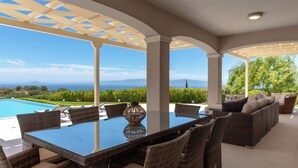 Un espacio de estar al aire libre cubierto con piscina, mobiliario de mimbre y vistas al mar y las montañas.