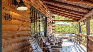 Een vakantiehuis in blokhutstijl met een veranda, waarop houten stoelen en een tafel staan. Op de muur is nummer 118 te zien.