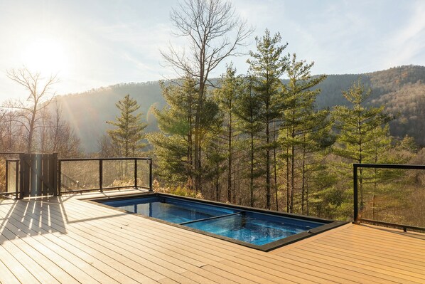 Eine Holzterrasse mit Schwimmbad, umgeben von Bäumen und Blick auf einen Berg.