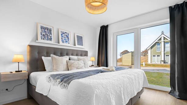 Una camera da letto moderna con un letto grande, comodini con lampade, un'ampia finestra con tende e un'opera d'arte appesa al muro.