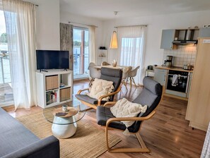 Una sala de estar moderna con un televisor de pantalla plana, un comedor con mesa y sillas, y una cocina con estufa y armarios.